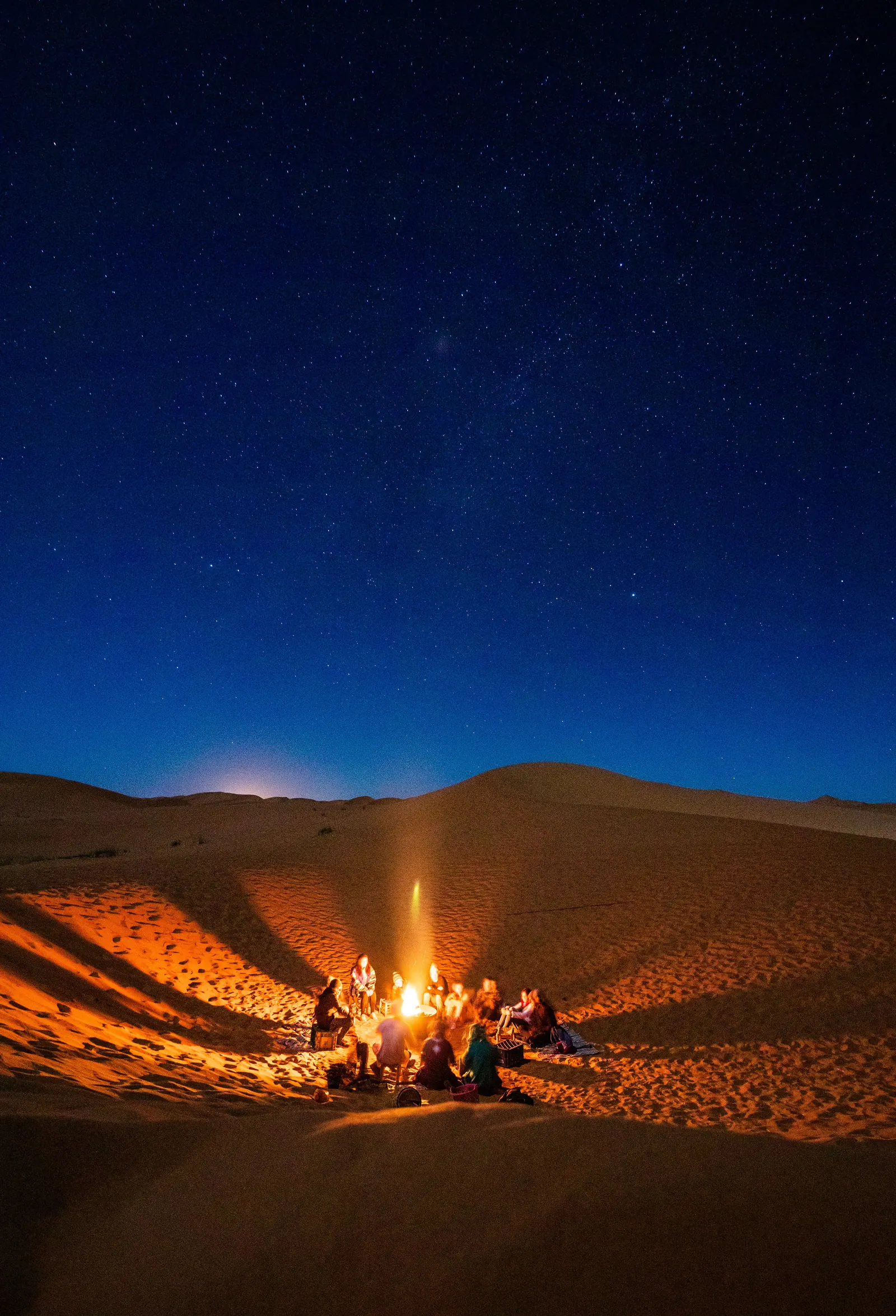 Group of travellers sitting around a campfire in the desert under a starry night sky